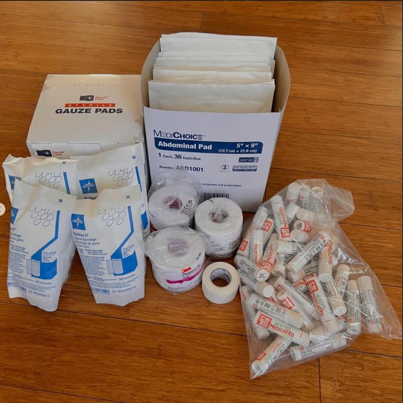 Gauze pads, abdominal pads, medical tape and lip balm donated by His Hands Free Clinic, laid out on a wooden floor