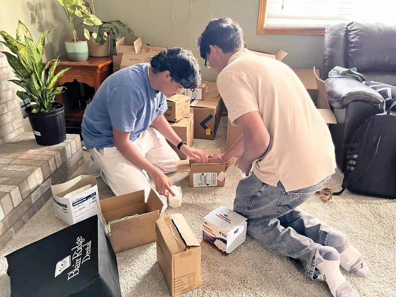 Our co-founders kneeling on the floor, packing gauze pads and hygiene supplies into boxes
